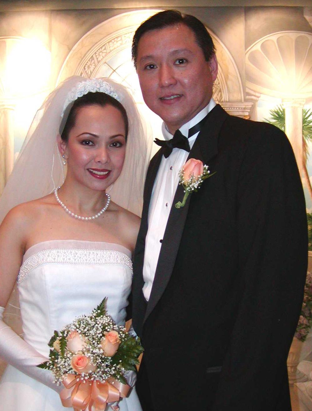 A smiling bride and groom with a peach rose bouquet